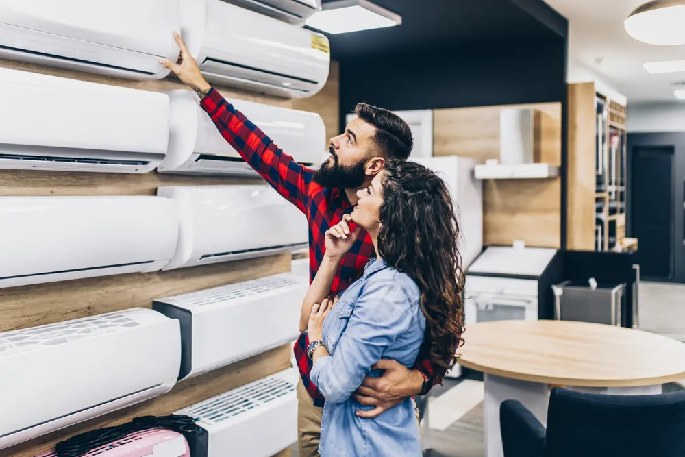 Casal escolhendo ar-condicionado em loja especializada, comparando modelos split e inverter para comprar o melhor aparelho na Black Friday 2025 Philco.